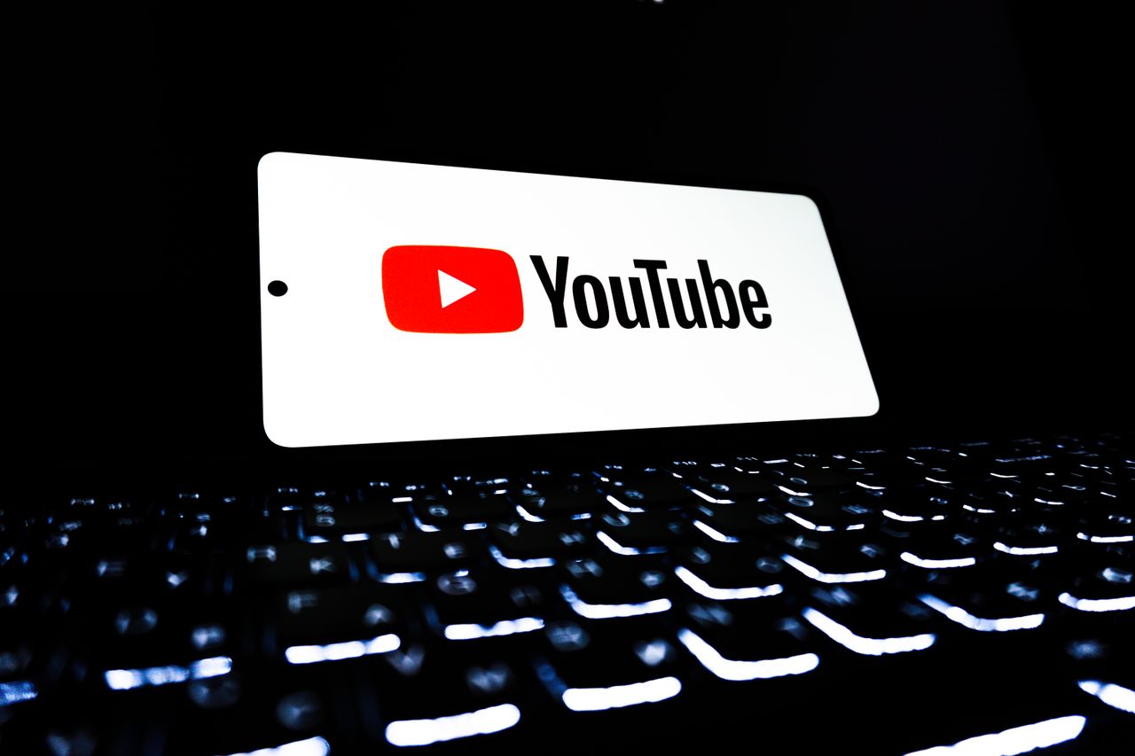 The YouTube app icon appears on a smartphone placed above a lit keyboard, symbolizing digital media and online streaming.
